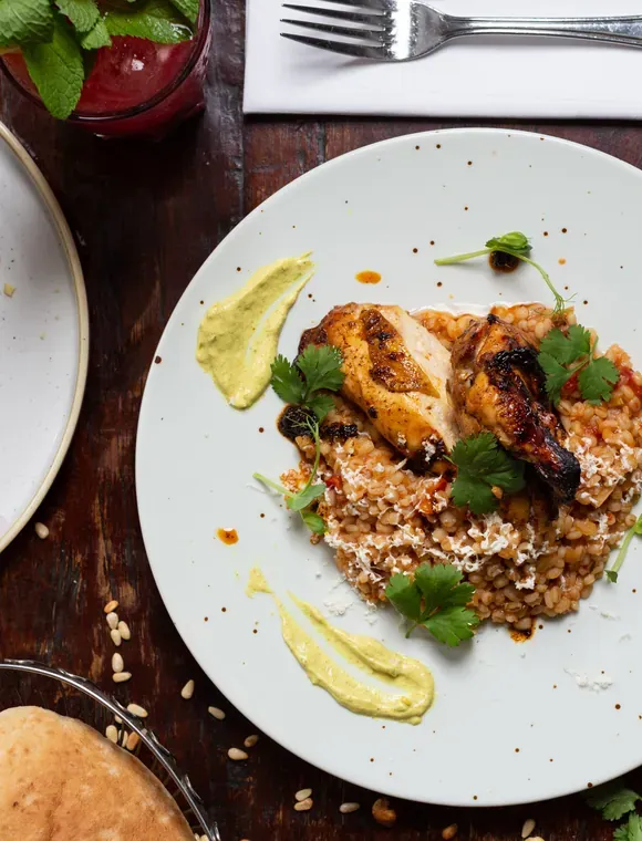 Teller mit Hähnchen, Bulgur und Kräutern auf einem Holztisch